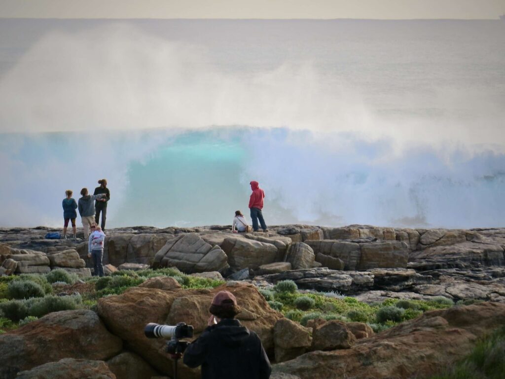 This images feature seven people who are looking towards mammoth waves.