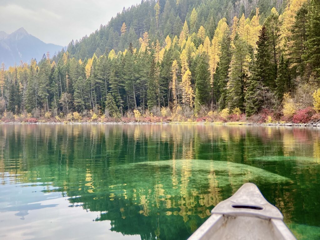 This image shows a canoe, sparkling lake waters and trees in the fall.