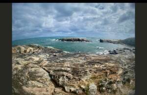Puffy cotton ball clouds and rocky terrain are showcased in this landscape image, revealing a glimpse of the mesmerizing ocean surrounding the Ozzie continent.